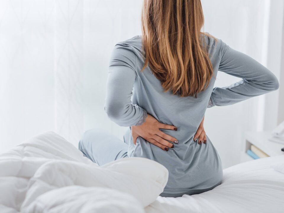 Kobieta na łóżku trzymająca się za bolące plecy