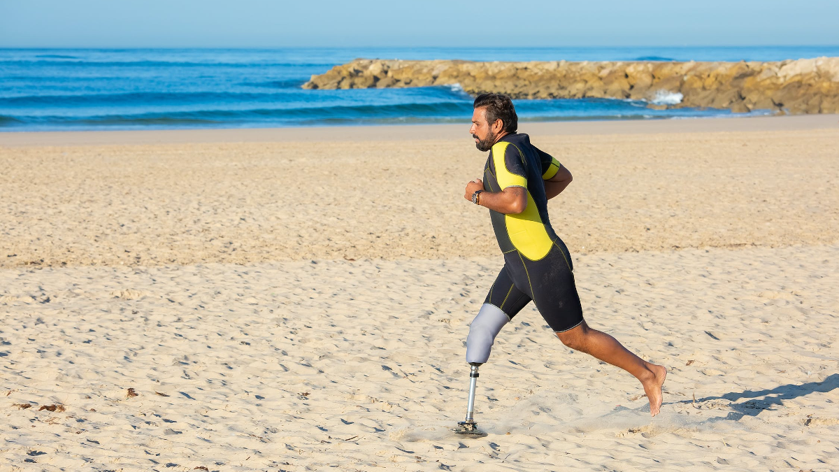 Surfer z protezą nogi biegnący po plaży